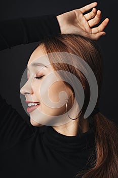 Side view close up - portrait of pretty beautiful young woman wearing black sweater isolate over dark background