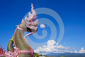 Side view of colorful traditional serpent statues on bannister of Thai temple against cloud on blue sky with beautiful rural scene