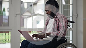 Side view concentrated African American disabled man in wheelchair surfing Internet in slow motion at home in living