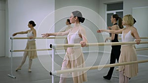 Side view concentrated ballerinas at barre rehearsing leg movement in studio indoors. Choreographer walking talking