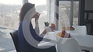 Side view of confident Caucasian woman smelling orange juice and taking fruit. Wealthy businesswoman having breakfast