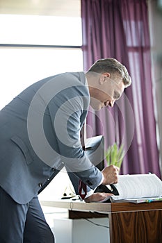 Side view of confident mature businessman reading book at desk in office