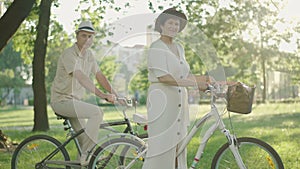 Side view of confident mid-adult couple posing with bikes in sunlight. Portrait of happy Caucasian man and woman looking