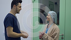 Side view of confident smiling Middle Eastern doctor and Caucasian patient standing in clinic corridor talking in slow