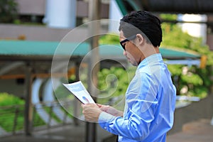 Side view of confident young Asian business man looking charts or paperwork and thinking his work in urban city background