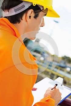 Side view of construction worker writing on clipboard at construction site