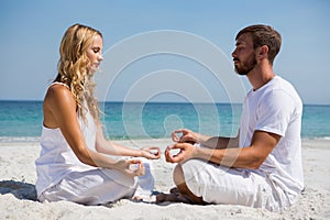 Side view of couple practicing meditation at beach