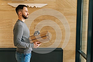 Side view of courier male holding boxes pizza and contactless payment POS wireless terminal, standing in entrance hall