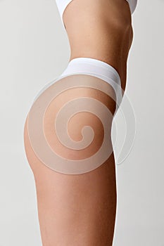 Side view of cropped female body in white inner wear isolated over light background. Anti-cellulite, care cosmetology