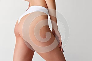 Side view of cropped sporty female body, buttocks in white inner wear isolated over light background. Anti-cellulite