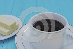 Side view cup of coffee and white chocolate wafer on a blue