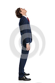 Side view of curious businessman in suit standing in line and looking up