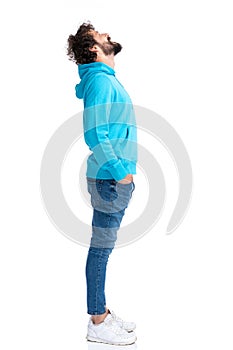 Side view of curly bearded guy holding hands in pockets and looking up
