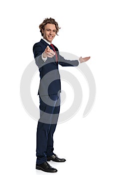 Side view of curly hair man in suit pointing fingers and inviting to side