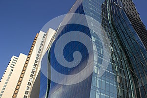 Side view of a curved blue glass window wall of a modern and elegant corporative building, next to a yellowish classical one.