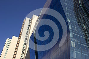 Side view of a curved blue glass window wall of a modern and elegant corporative building, next to a yellowish classical one.