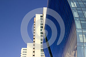 Side view of a curved blue glass window wall of a modern and elegant corporative high-rise building, next to a yellowish classical