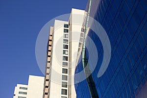 Side view of a curved blue glass window wall of a modern and elegant corporative high-rise building, next to a yellowish classical