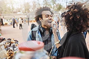 Side-view of cute african-american couple in love having fun in park during food festival, standing near counter and