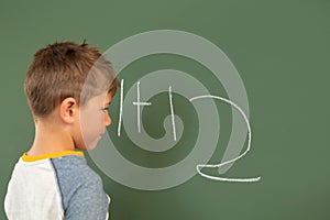 Schoolboy doing math on green chalkboard in a classroom