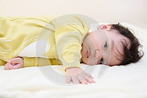 Side view of a cute little Asian babe Wearing a yellow dress, lying on the bed and look at camera