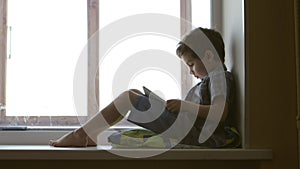 SIDE VIEW: Cute little boy uses a white tablet PC on a windowsill at home - middle shot