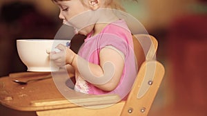 Side view of cute little girl eating soup or muesli from bowl.