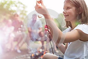 Side view of cute smiling girl holding stick and marshmallow at campsite in park