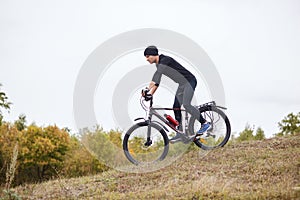 Side view of cyclist riding mountain bike downhill, extreme sports on bicycle outdoors, young sportsman wearing black sportsuit