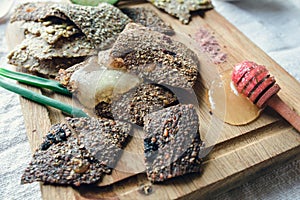 Side view of dark linen breads, honey dipper and green onions served on vintage wooden board