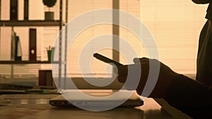 Side view dark silhouette of a man typing on a laptop keyboard and then texting on his mobile phone. A male manager