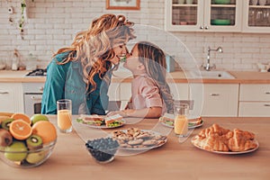 Side view of daughter and mother touching noses while sitting at the kitchen table with food