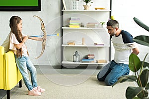 side view of daughter playing with tied father and pretending shooting with toy bow