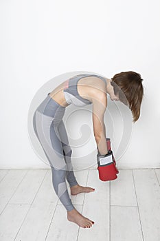 Side view on defeated female boxer in sportswear and boxing gloves standing on the floor close to the wall