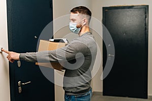 Side view of delivery man wearing medical mask holding cardboard box and contactless payment POS wireless terminal for