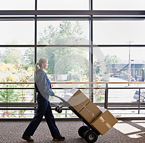 Side view of delivery woman pushing stack of boxes