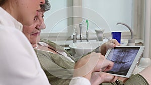 Side view of dentist showing X-ray of teeth on tablet to her patient