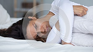 Depressed young mixed race woman lying on bed in bedroom, embracing knees.