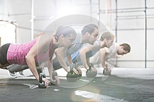 Side view of determined people doing pushups with kettlebells at crossfit gym