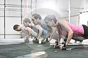 Side view of determined people doing pushups with kettlebells at crossfit gym