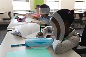 Side view of disable black schoolgirl studying and sitting at desk in classroom