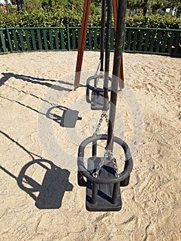 Side view of double swing bench with metal ropes on sand ground of playground. Closeup of empty swing on children playground.