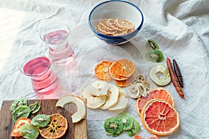 Side view of dried fruits slices in a bowl and on wooden board, fruit candy rolls and two glasses of vitamin water on linen cloth
