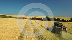 Side view from a drone of a combine harvester working in a wheat field. The harvester agricultural machine harvests a