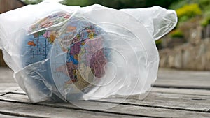 Side view of the Earth in polyethylene disposable package on wooden background. Concept of ecological problems. Stop