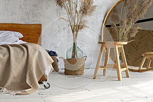 Side view of eco style loft bedroom with  wooden chair, mirror and pampas grass decoration