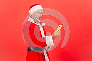 Side view of elderly man with gray beard wearing santa claus costume standing with open mouth and