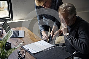 Side view of elderly man sitting on wheelchair looking at life insurance contract form