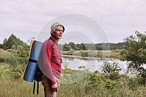 Side view of eldery man with backpack and blue rug, enjoying of admiring majestic view of river while walking in wonderful