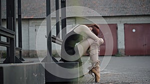 Side view of elegant slim ballerina with ropes on legs hugging knees. Young Caucasian woman in black dress and yellow